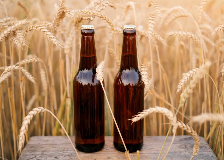 Two brown bottles on a table set against a wheat field backdrop