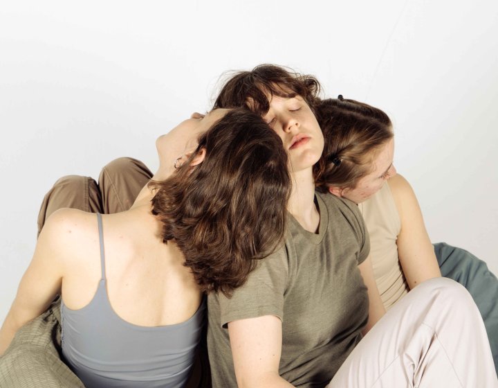A group of dancers on the floor huddled together against a very light grey backdrop