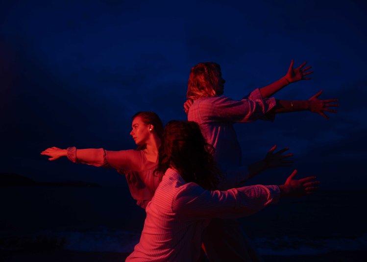 A dark and moody image of 3 dancers performing outside with a red light on them