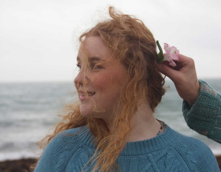 a person looking to the right wearing a blue jumper on a black with a flower being held in their hair