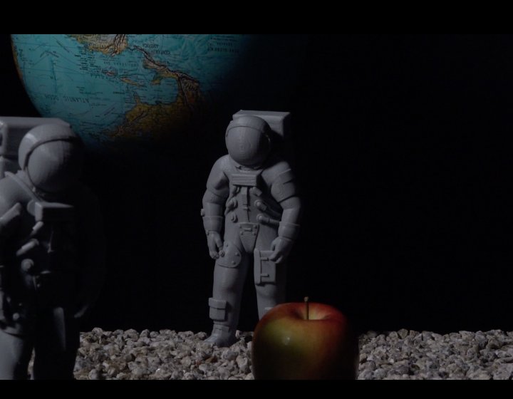 A globe with two plastic figurines and an apple in the front of the image