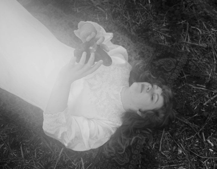 A black and white image of a person laying on the floor in a white dress holding an object