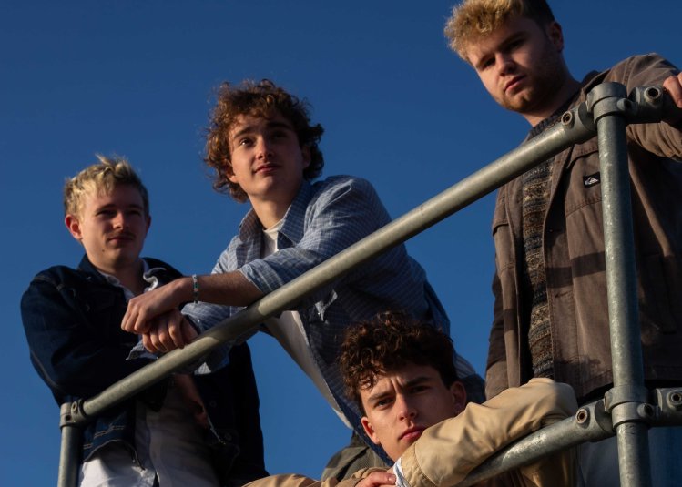 A group of 4 leaning against a metal bar with blue sky in the background