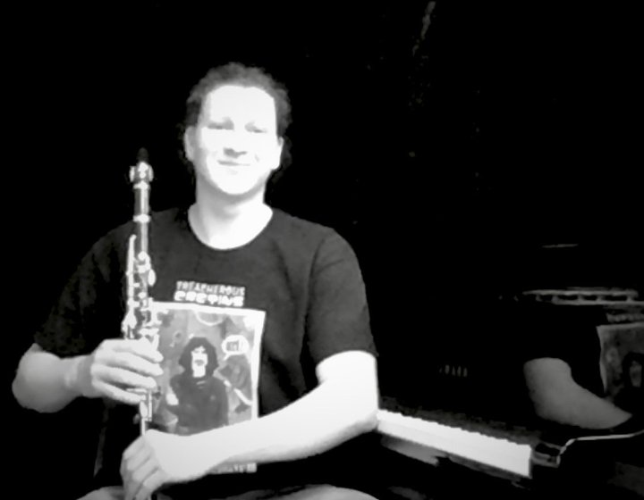 A black and white image of a person sat down with a clarinet on their knee