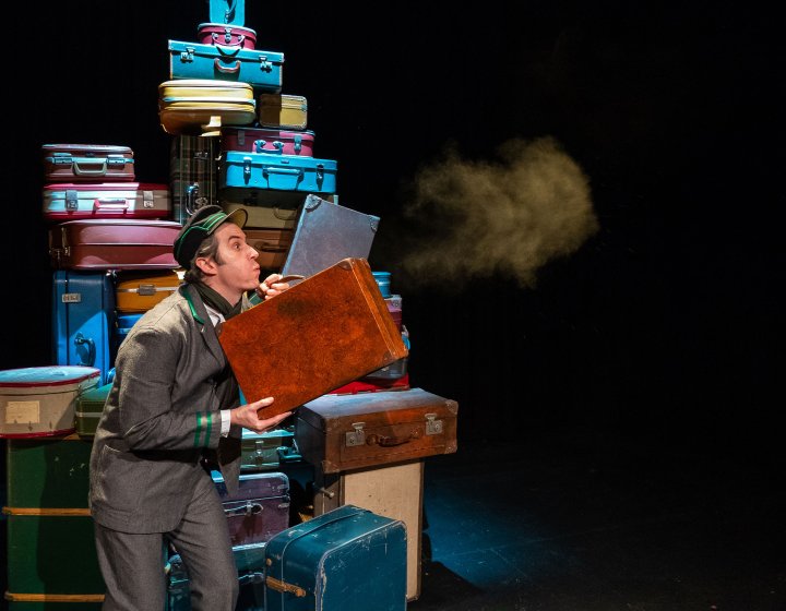 A person stood in front of a big pile of suitcase blowing dust off on one into the distance