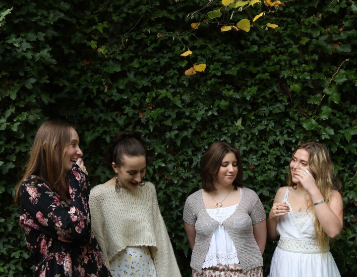 Four singers in a line against a green tree