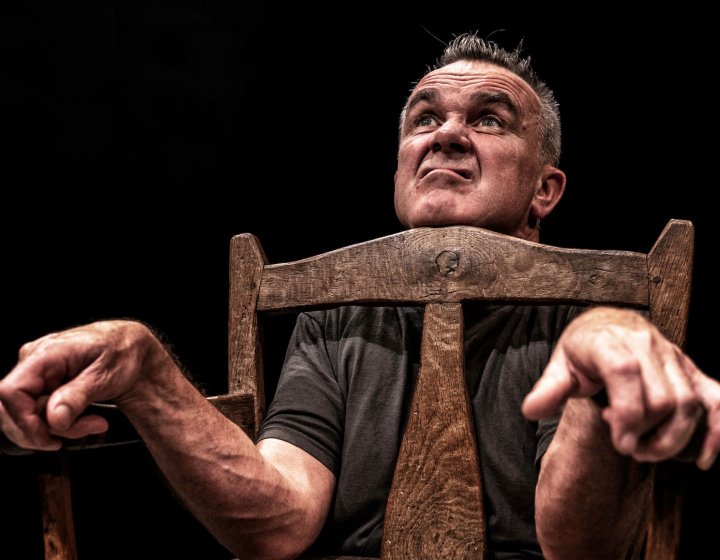 A man pulling a silly afce looking with chin resting on a chair