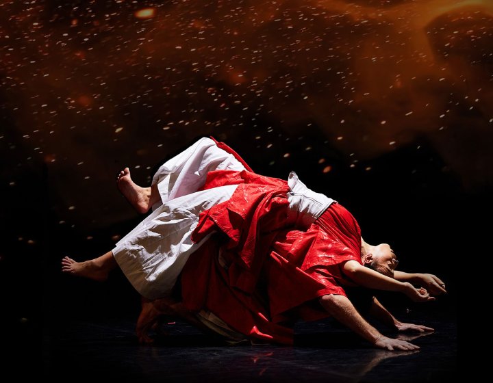 Two dancers performing in white and red outfits with a dark and moody black and red background