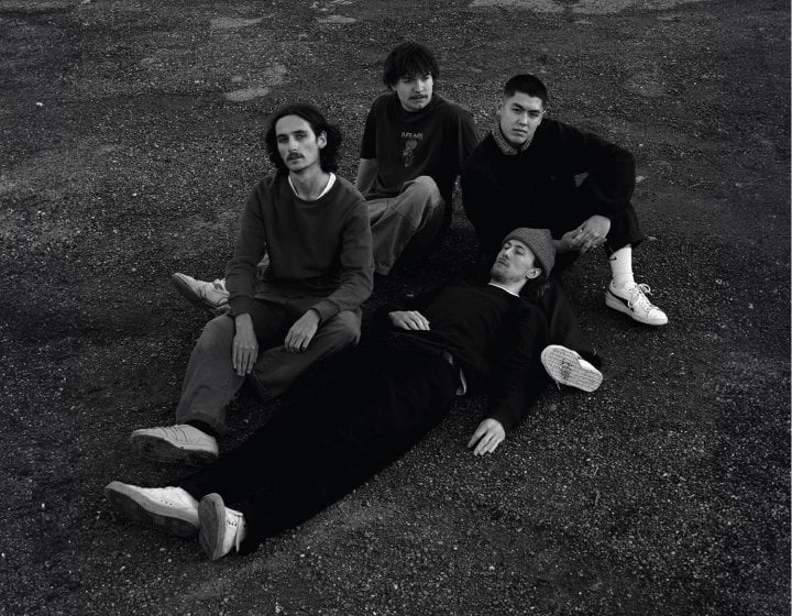 Four people sitting on the grass in a black and white image looking up into the air at the camera