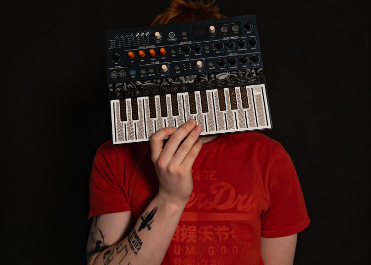 A person wearing a red t-short holding a small midi keyboard in front of their face