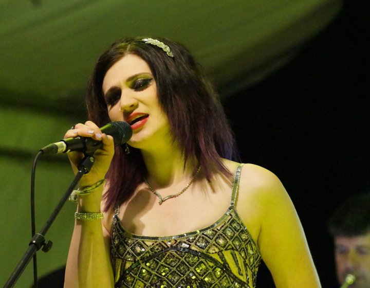 A female singer holding a microphone whilst performing with a green lit background