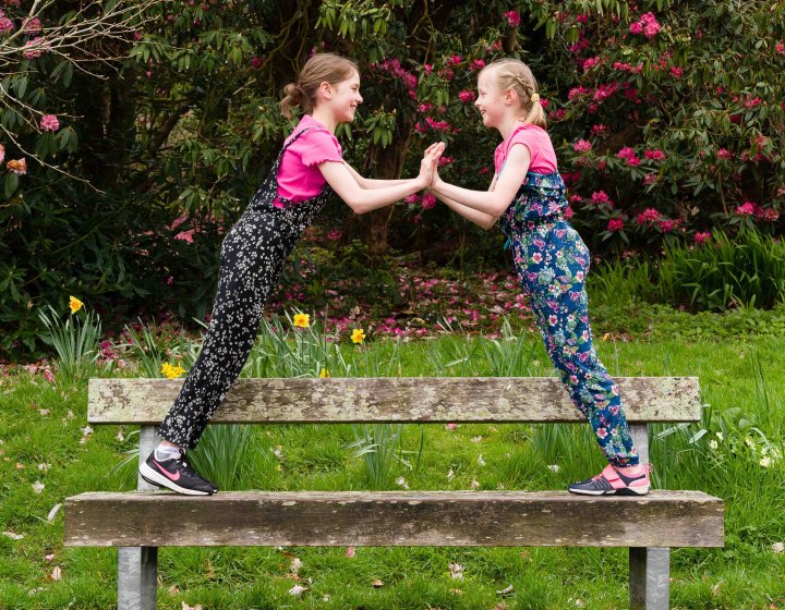 Two young dancers leaning towards each other on a bench in front of bushes and grass