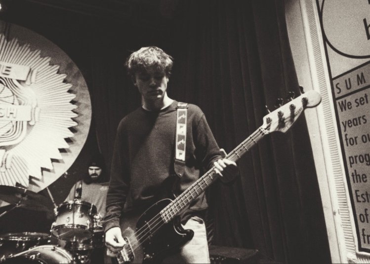 A black and white photo a someone performing on stage playing the bass guitar