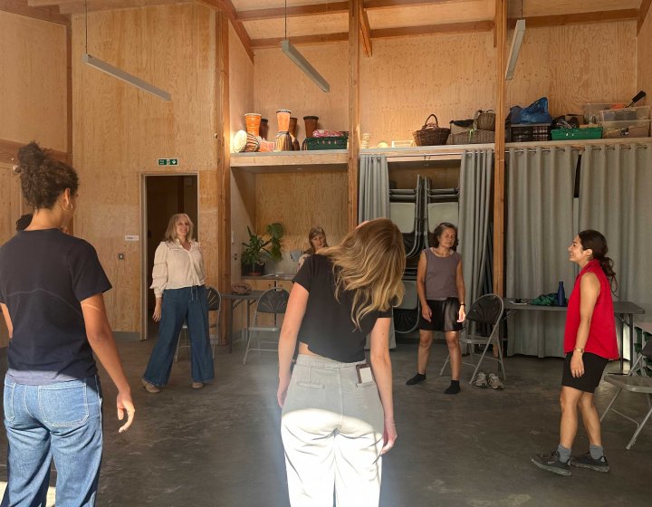 A group of performers in a theatre workshop anwooden room with a green floor