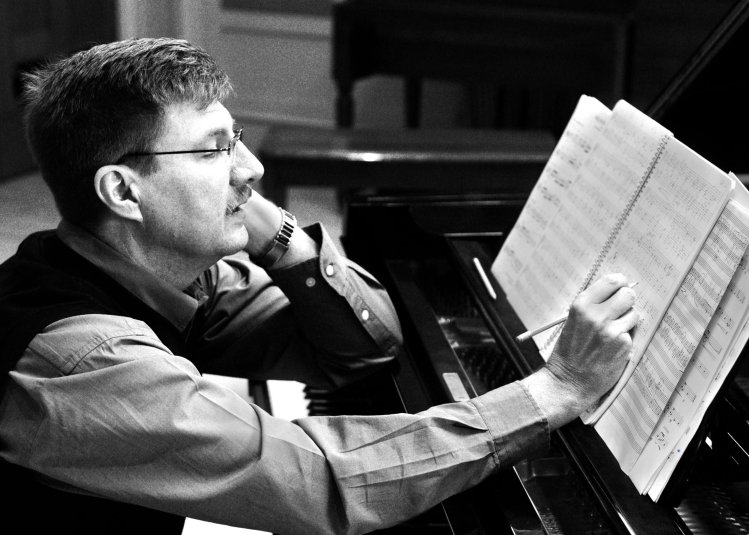 A black and white photo of a composer sat at a piano