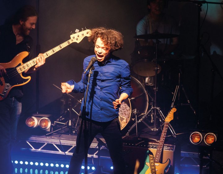Student singing and jumping on stage in front of guitarist