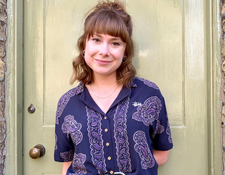 A woman in front of a door wearing a purple shirt