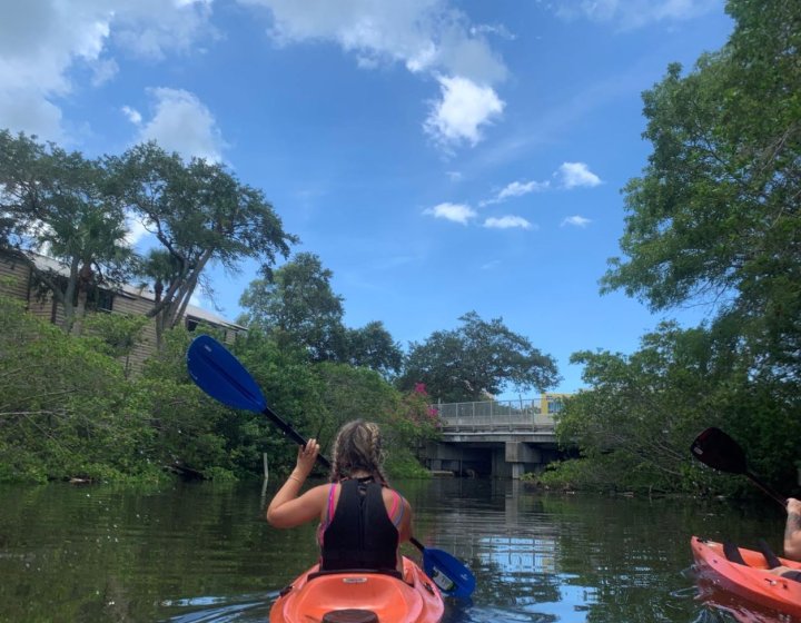 A girl in an orange kayak on the water with trees