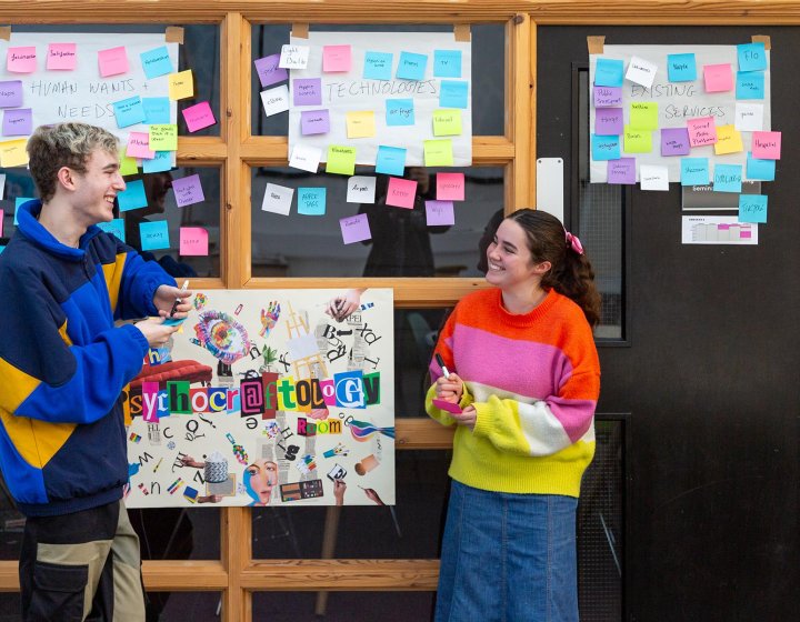 Two Falmouth University Creative Advertising students discussing ideas with post-it notes on a board