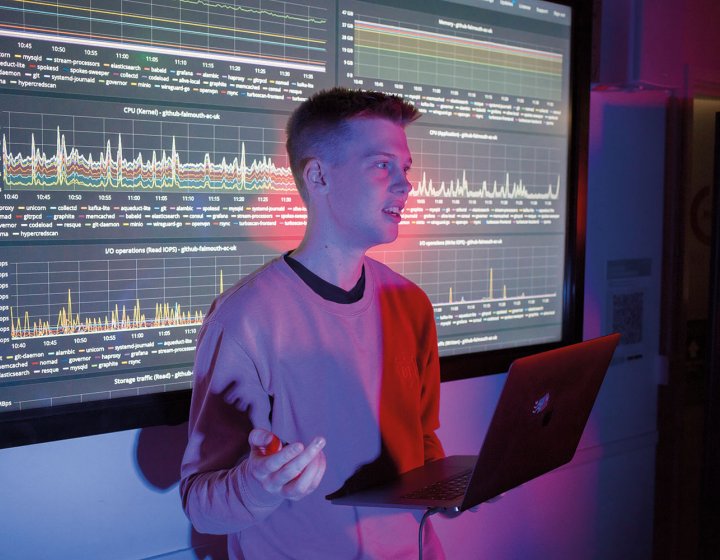 Student stood in front of large screen with code and graphs on