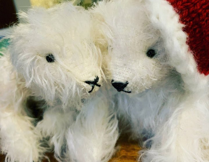 Two white mohair bears, one wearing a red santa hat