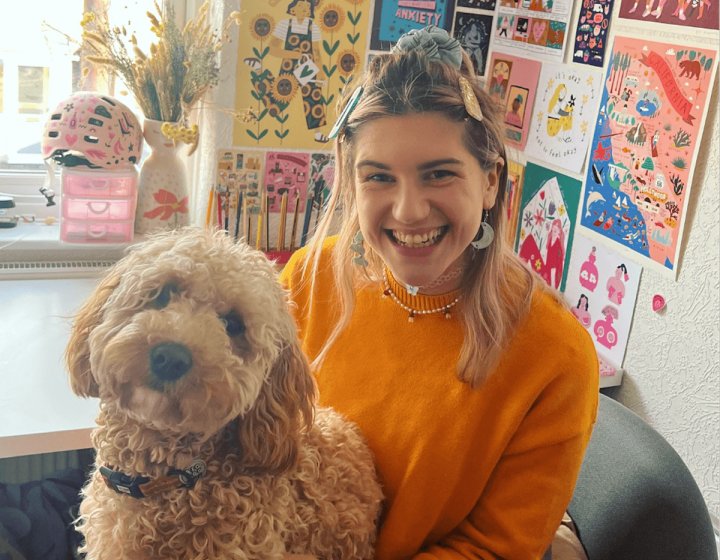 A young woman wearing an orange jumper with a dog on her lap