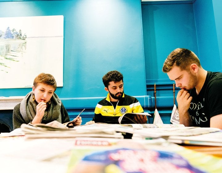 Students reading newspapers around a desk