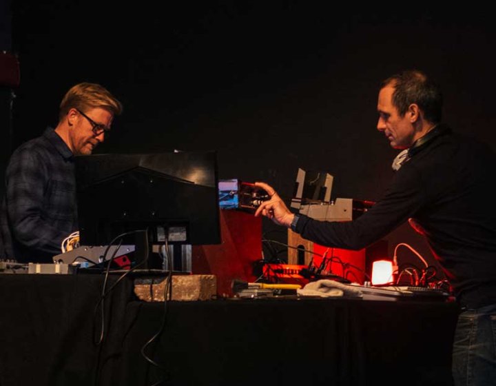 Two men on a stage using analogue equipment to perform a live film score