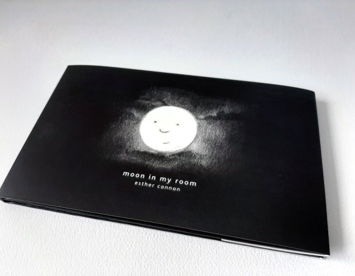 Photo of a book cover - illustrated moon with face on a black background and the title 'Moon in my Room' in white.