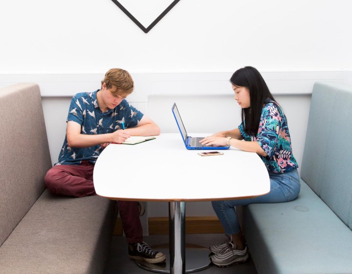 Two Falmouth University students working at a white table with sofas