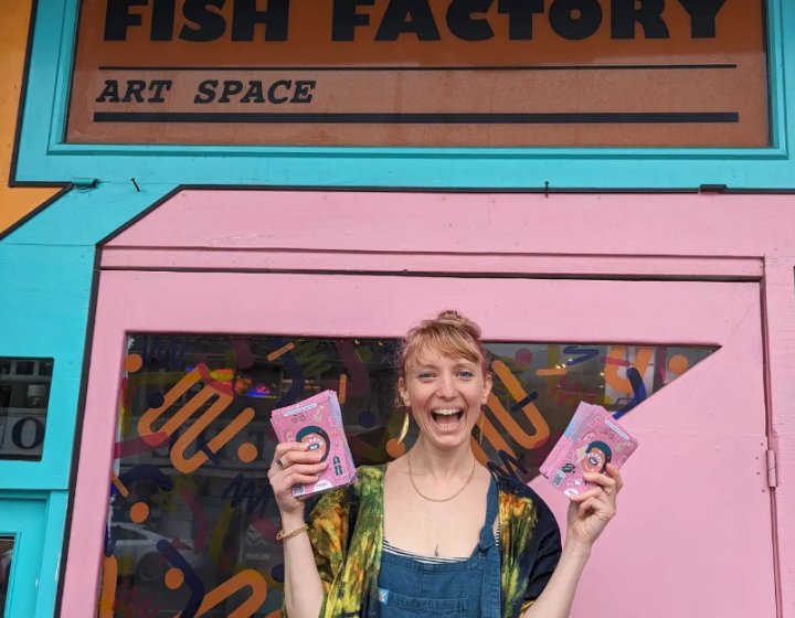A woman stood outside a pink building holding maps