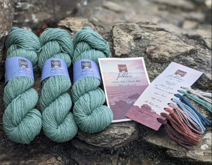 Three spools of green yarn and card holding various colours of yarn on rocks at the beach