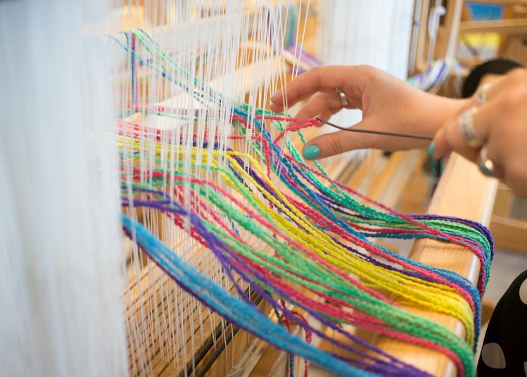 A hand using a weaving machine with multi-coloured wool