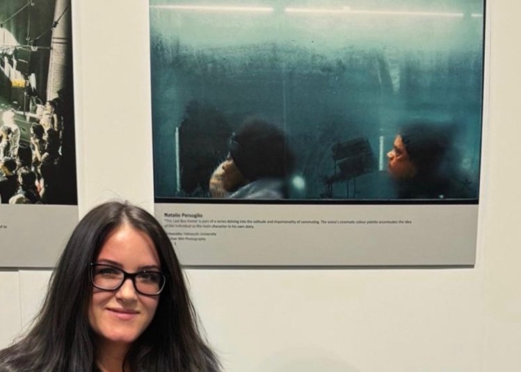 Photography student Natalie Persoglio standing next to her award-winning image of two people on a bus