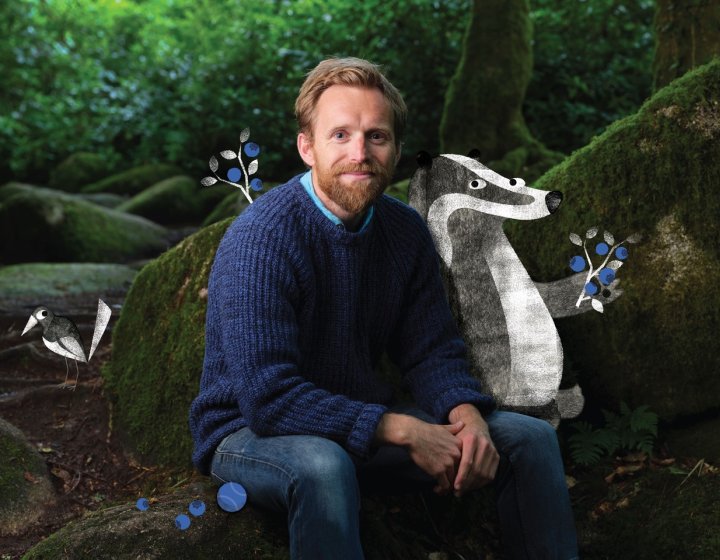Huw Lewis Jones sitting in the woods with an illustration of a badger, bird and flowers