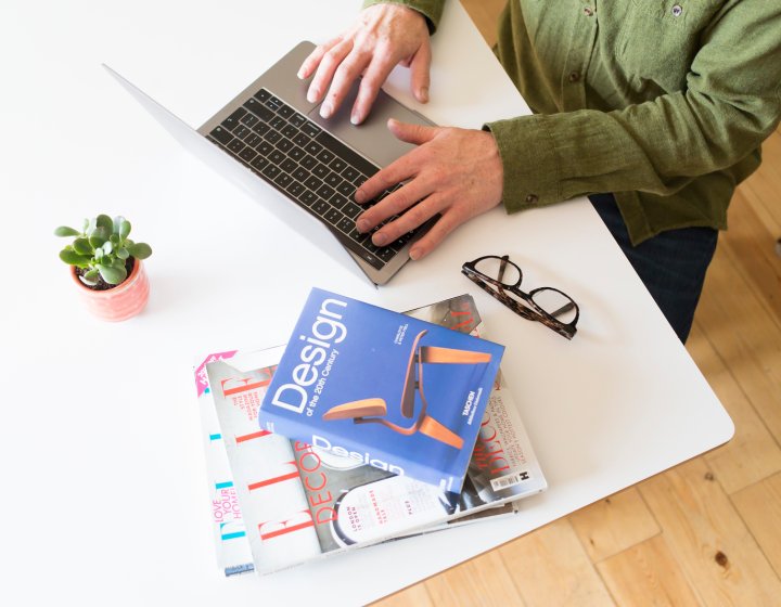 A student working at their desk with a laptop and a pile of books 