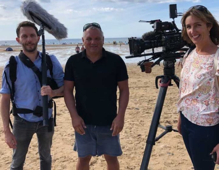 Three people stood on a beach with cameras and filming equipment
