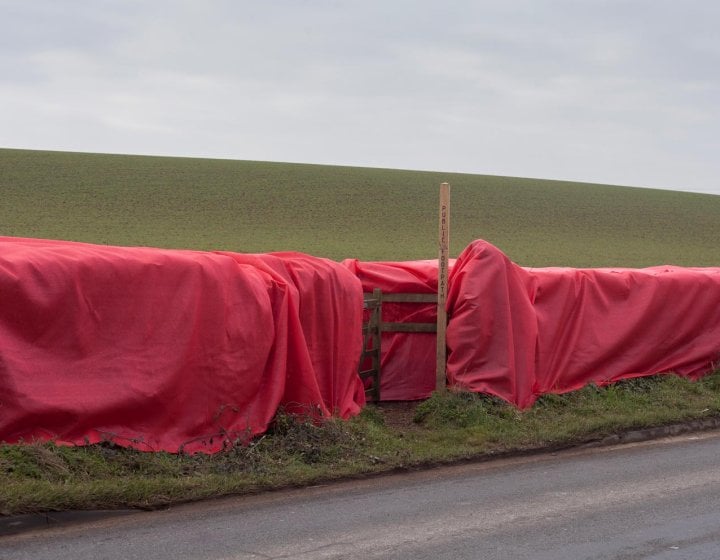 Large red material draped over a wooden fence with a public footpath sign