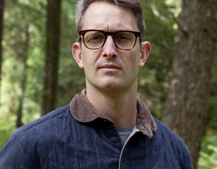 A man wearing glasses stood in a woodland 