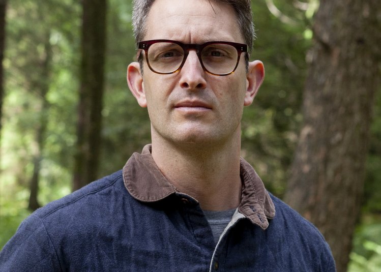A man wearing glasses stood in a woodland 