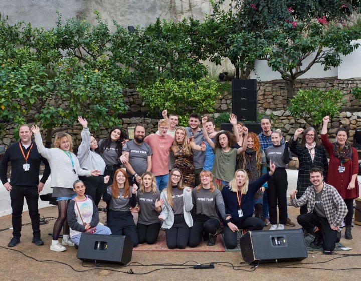 A large group of Sustainable Festival Management students posing in front of a wall with speakers on the floor