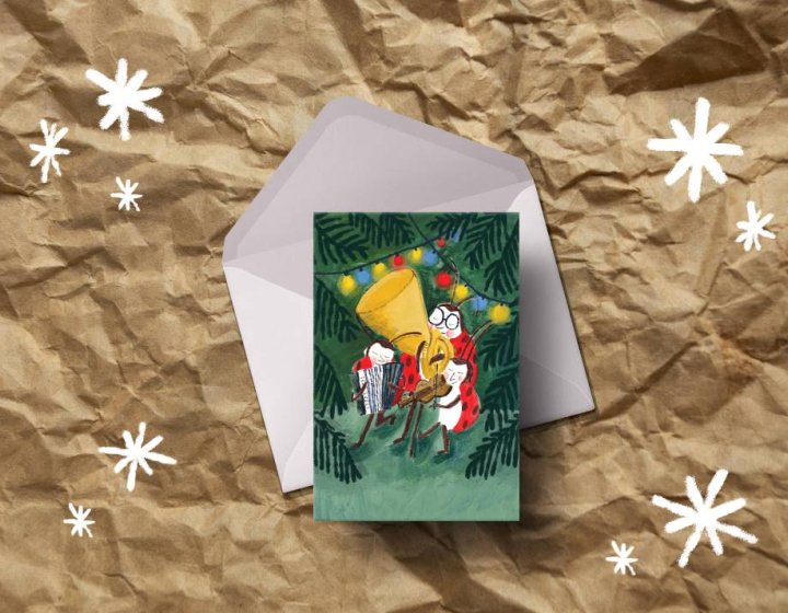 Photo of illustrated Christmas card, featuring ladybirds, laying on white envelope with crumpled brown paper background