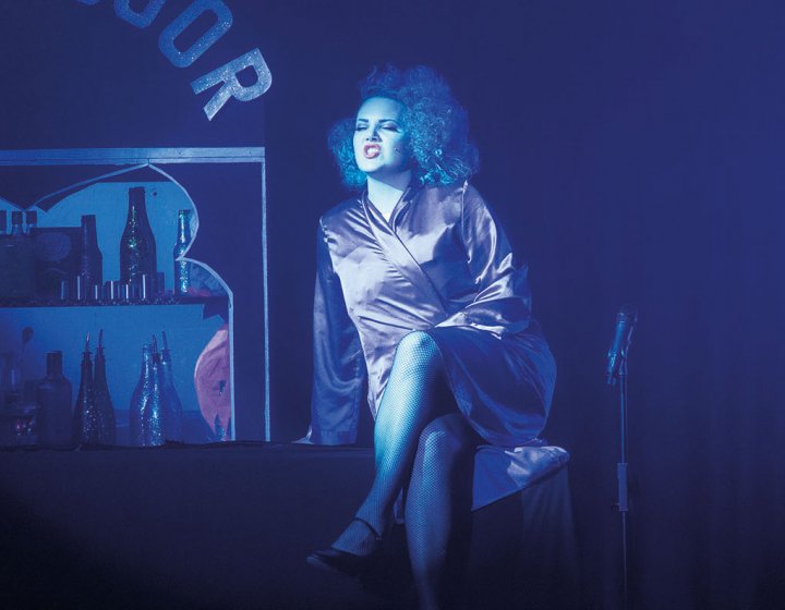 Student on stage in blue lighting and silk gown