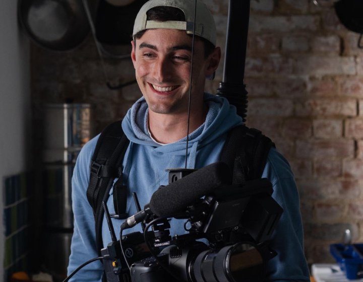 A young man in a backwards cap holding a large camera