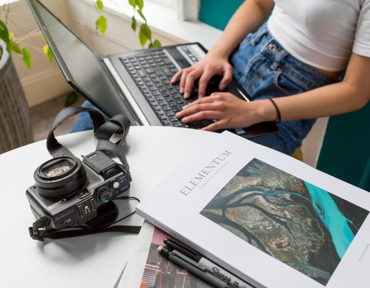 A desk with a stack of books, acamera and a laptop