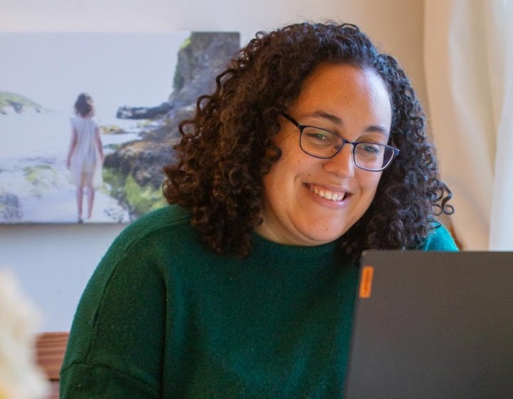 A woman with curly hair and glasses laughing at a laptop
