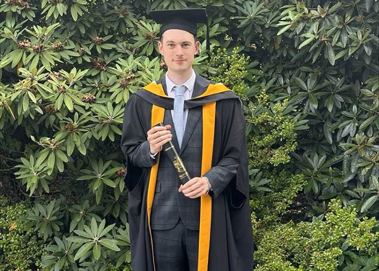 User Experience Design graduate Paul Phillips at graduation wearing a gown and mortar board