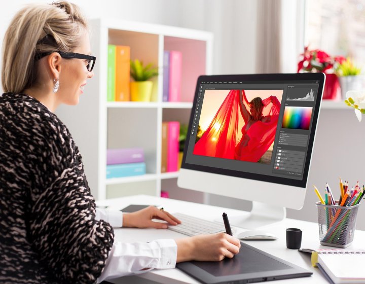 A woman working on an iMac editing a photograph of a woman in a red shawl