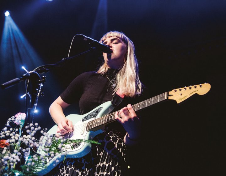 Student singing into microphone on stage and playing guitar
