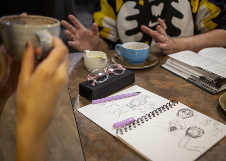 A photo of two students drinking coffee with drawings on the table